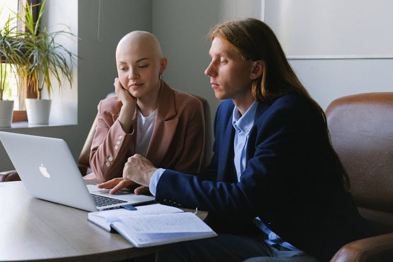 Two colleagues having a focused business discussion using a laptop in an office setting.